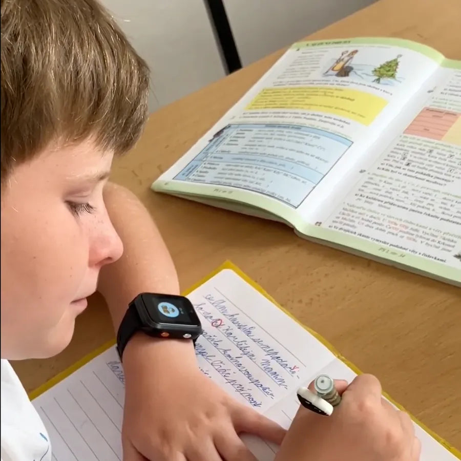 Écolier portant la montre KLOKI à son bureau en classe.